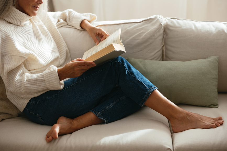 middle aged woman sitting on couch reading a book
