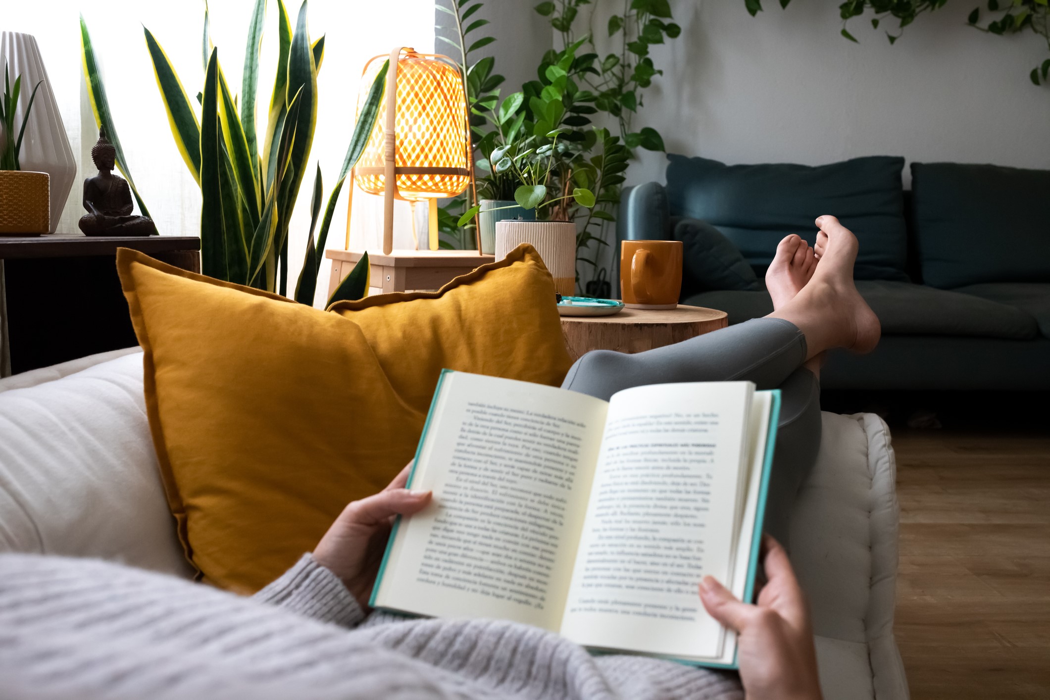middle aged woman reading a book while laying on her couch