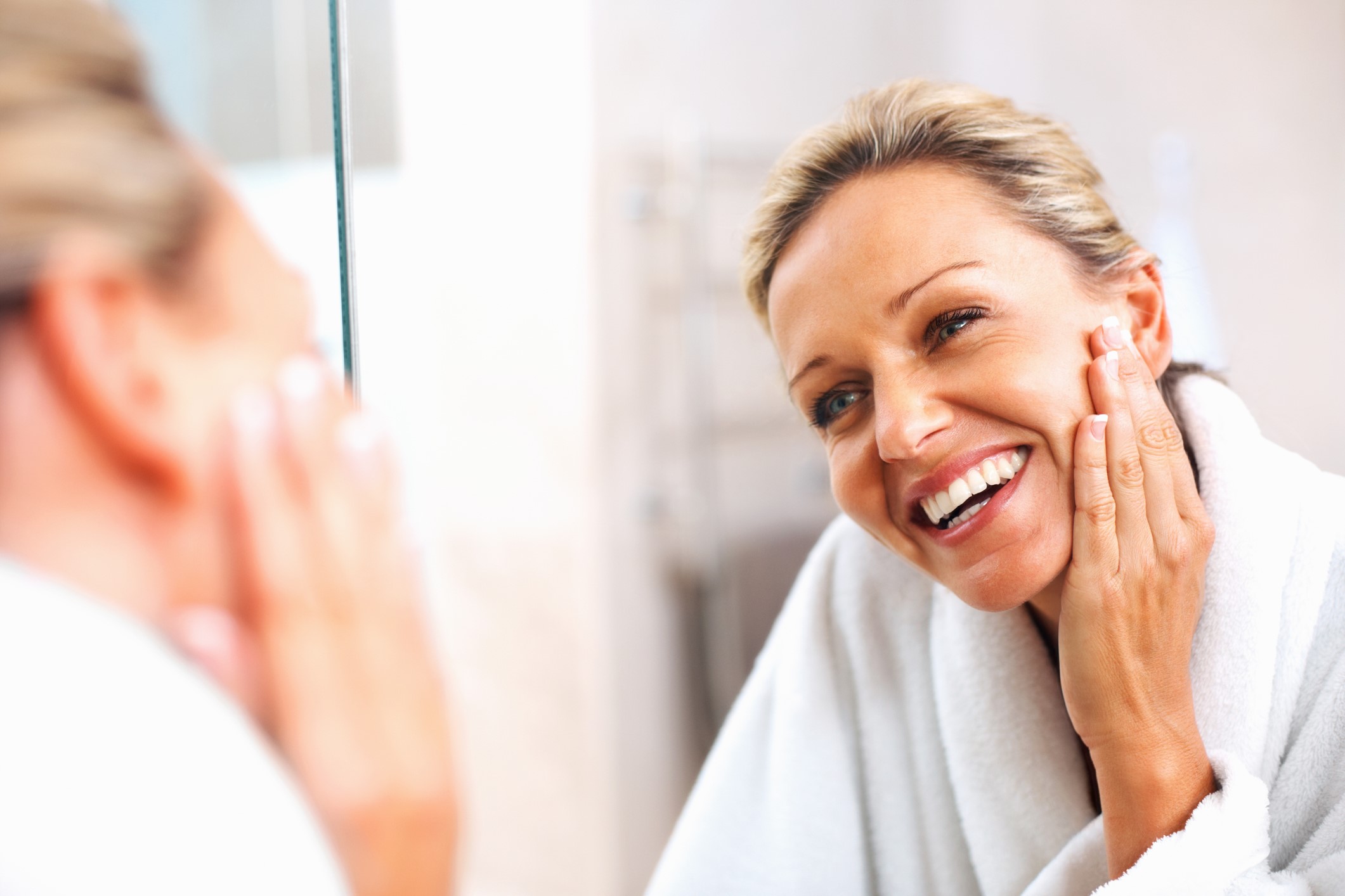 middle aged woman applying anti-aging serum while looking in mirror.